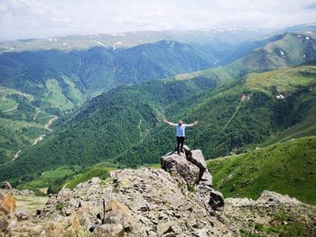 Man spreading arms while standing on rock against mountains