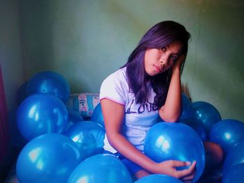 Portrait of young woman with blue balloons sitting at home