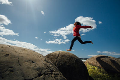 Low angle view of man jumping on rock against sky