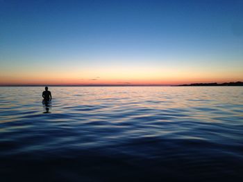 Silhouette man standing in sea against sky during sunset