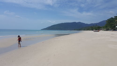 Woman walking at beach against sky