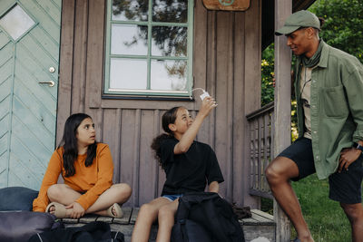 Girl showing portable charger to male counselor standing near cabin at summer camp