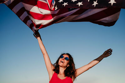 Low angle view of woman with american flag against clear blue sky