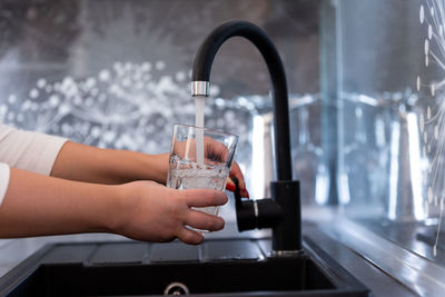 Hands of a young woman pouring a glass of water in a modern kitchen