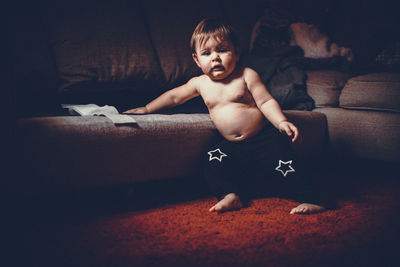 Portrait of shirtless baby boy standing by sofa at home