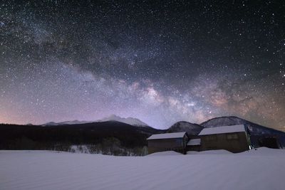 Houses on snowcapped field against star field in dramatic sky