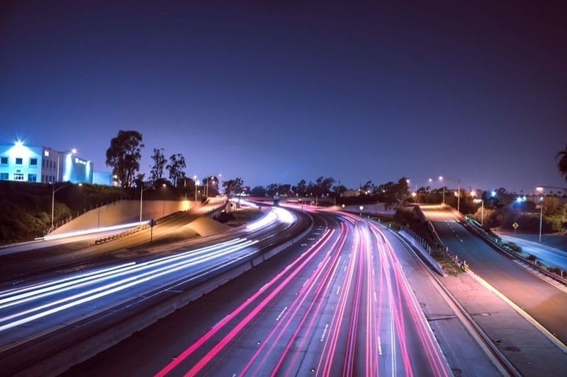 illuminated, light trail, night, long exposure, motion, building exterior, speed, city, road, blurred motion, architecture, built structure, transportation, clear sky, street, traffic, city life, car, multi colored, high angle view