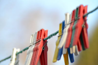 Close-up of clothespins hanging from rope against sky