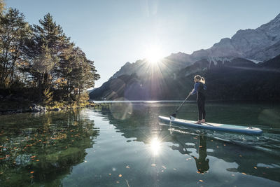 Germany, bavaria, garmisch partenkirchen, young woman stand up paddling on lake eibsee