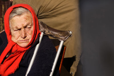 Ukrainian elderly woman in red shawl with crutches sitting outside. woman 80 years old. alone 