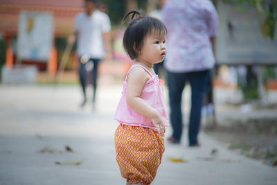 Cute baby girl looking away while standing on footpath