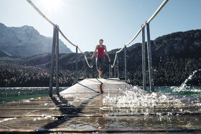 Young woman walking on pier against clear sky during sunny day