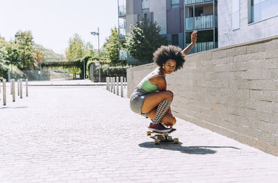 Young woman crouching on skateboard outside building