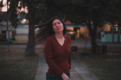 Mid adult woman looking away while standing against trees in park during sunset