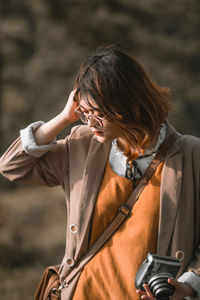 Young woman holding camera while standing outdoors