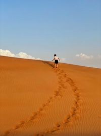 Man on sand dune in desert against sky