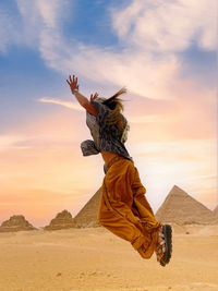 Rear view of woman with arms raised standing on sand at desert