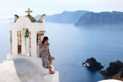 Woman leaning by cross against sea at santorini