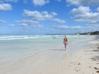 Rear view of woman walking on beach against sky