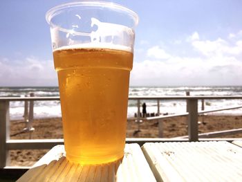 Close-up of beer glass on table against sea
