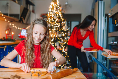 Mother and daughter preparing food against illuminated christmas tree