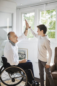 Disabled man in wheelchair giving high-five to son at home