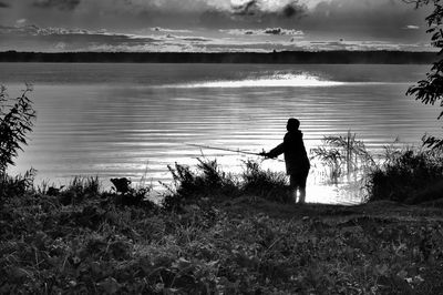 Silhouette man standing by lake against sky
