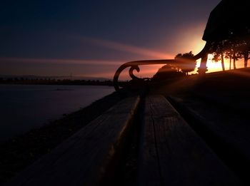 Silhouette railing by sea against sky during sunset