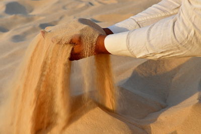 Cropped hands of man holding sand at desert