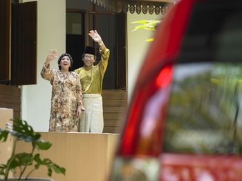 Couple waving while standing outside house