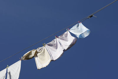 Low angle view of clothes hanging on rope against clear blue sky