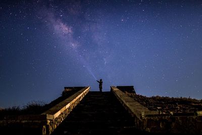 Low angle view of steps leading towards man against star field at night