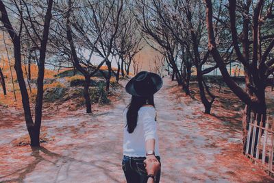 Cropped image of boyfriend holding girlfriend hand on road amidst trees in park