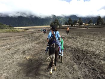 People riding horses on beach against sky