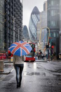 Rear view of woman holding umbrella standing on wet street