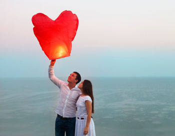 Woman standing by heart shape against sea against sky