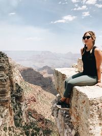 Portrait of woman sitting on cliff against sky