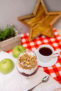 Cherry yoghurt parfait with crispy granola on top in a wine glass and cup of tea