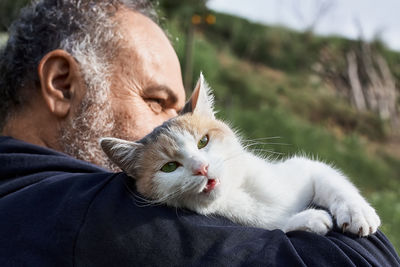 Tricolor cute cat meows on mature man's shoulder. friendship, love, love of animals