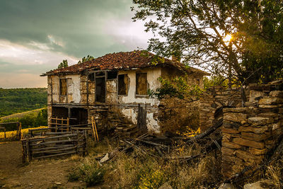 Abandoned house on field against cloudy sky