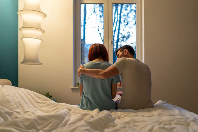 Rear view of woman sitting on bed at home