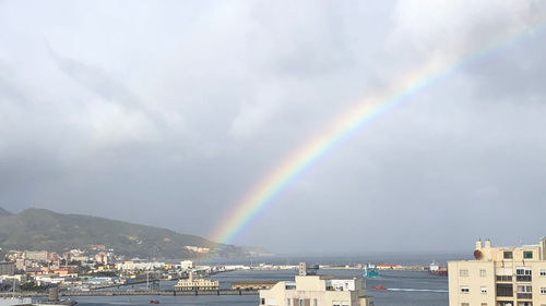 Rainbow over city by sea against sky