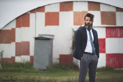 Hipster with hands in pockets on field against barn