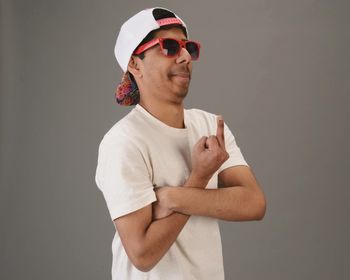 Man in sunglasses gesturing obscene gesture against gray background