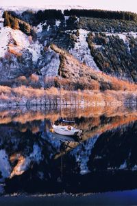 Boat moored in lake against mountains during winter