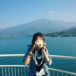 Woman photographing with instant camera while standing against sun moon lake