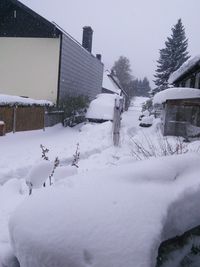 Close-up of snow covered road by houses against sky