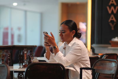 Young woman using mobile phone while sitting in cafe