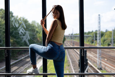 Portrait of young woman standing by railing against window