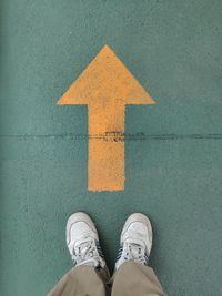 Low section of man standing on arrow sign